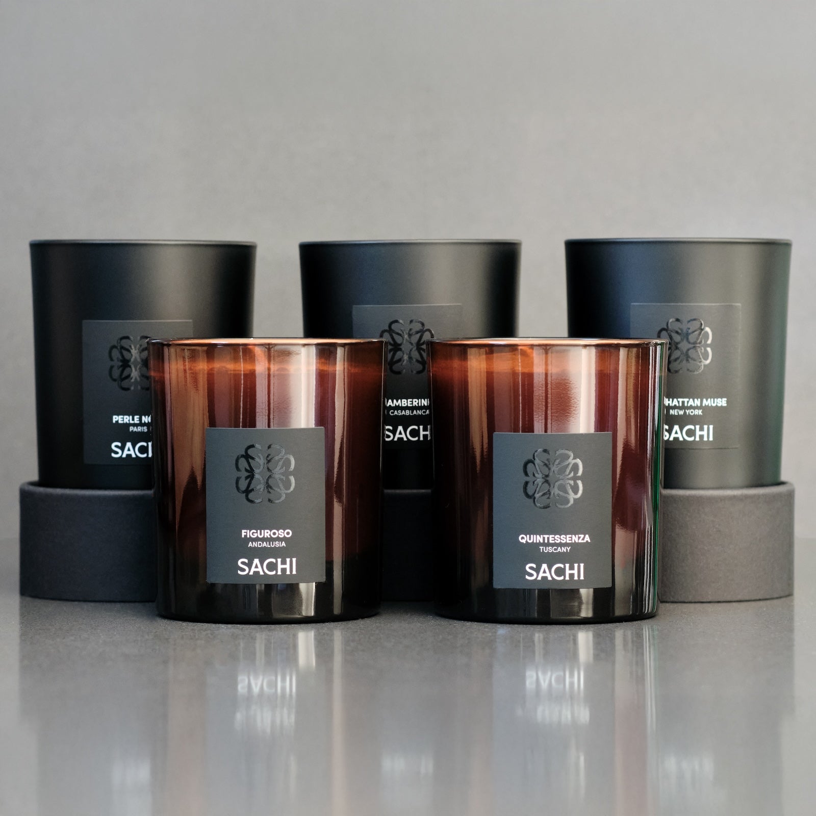 Set of Sachi candles in various designs on a reflective surface with a neutral background