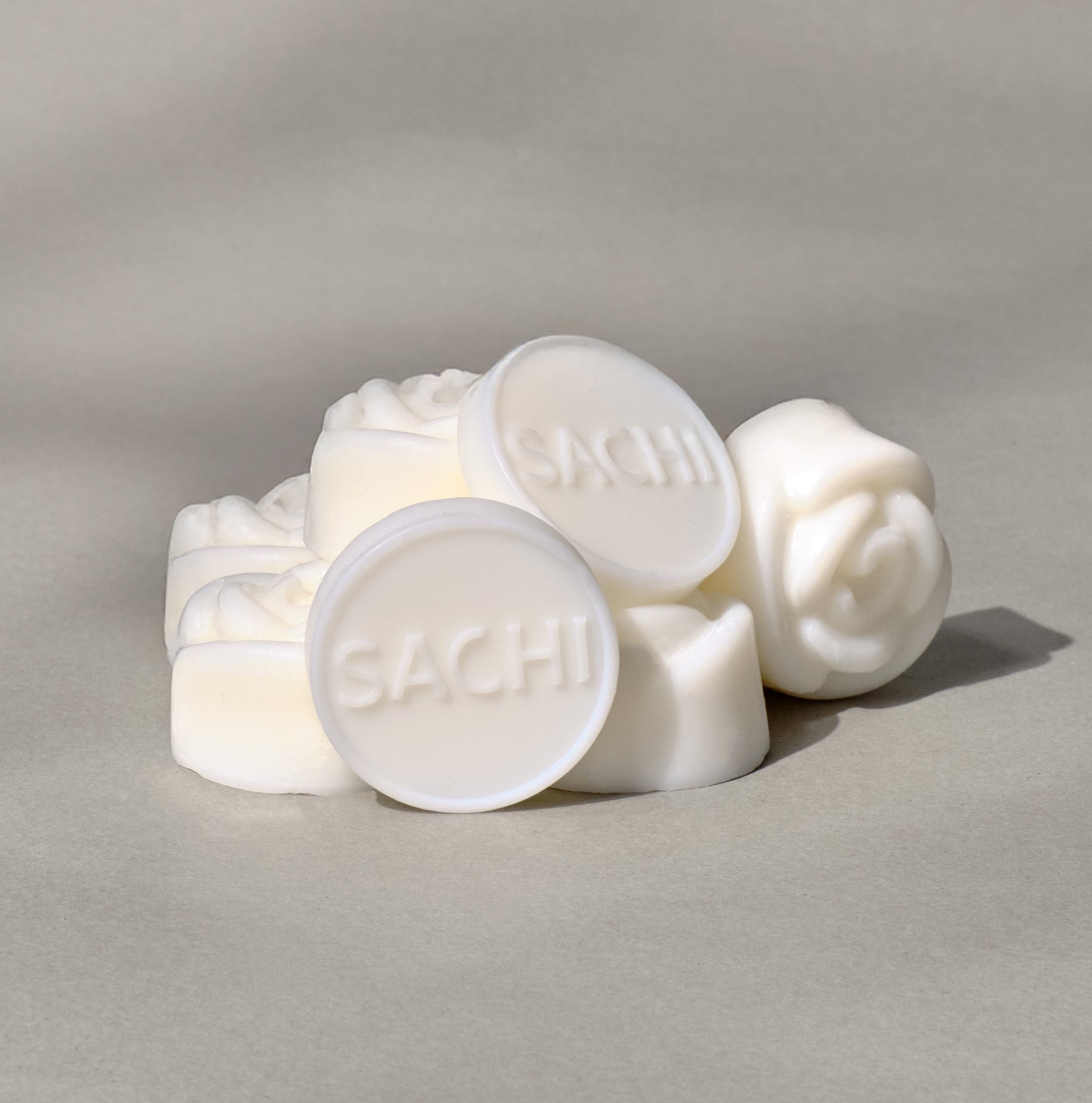 A pile of ivory wax melts with the brand name 'SACHI' imprinted on some, placed on a neutral background.