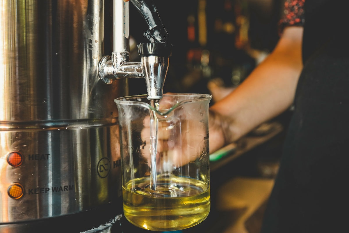 Liquid wax being poured from a metallic container into a glass measuring jug