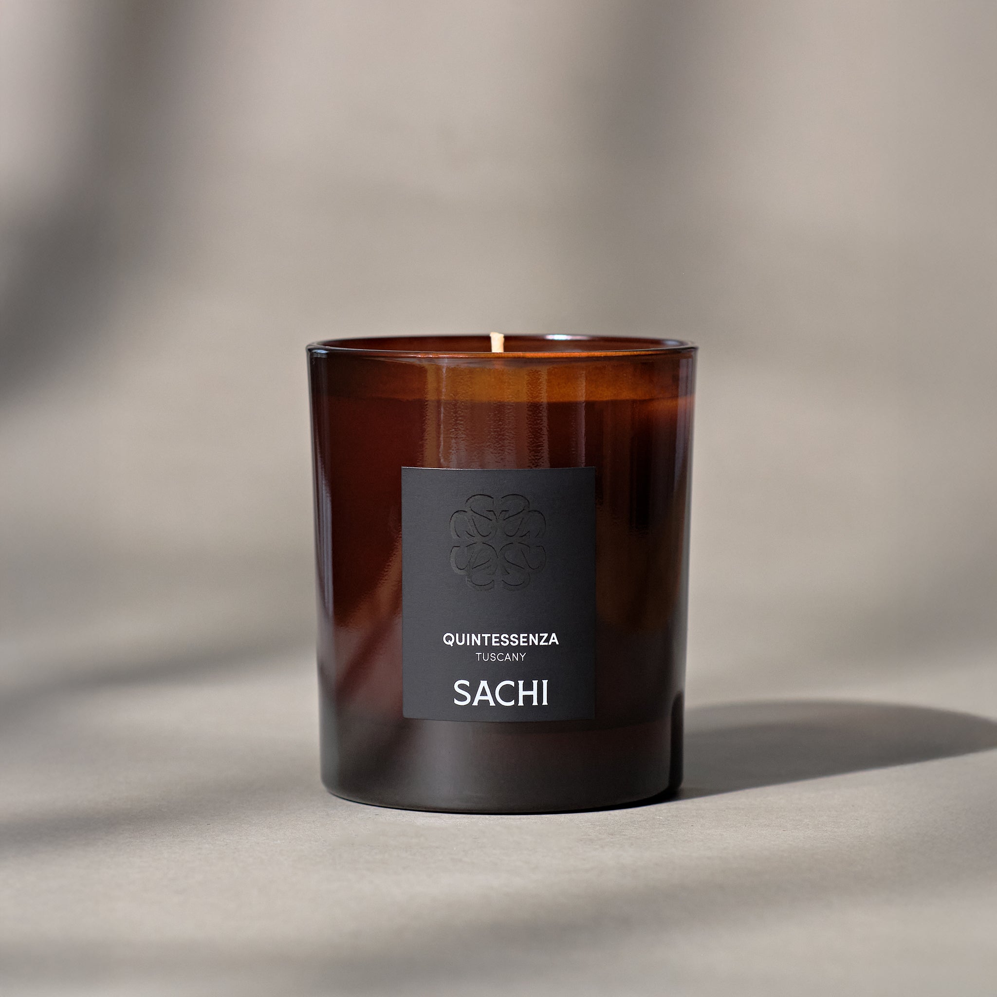 An amber glass candle jar with a black label, featuring the text 'QUINTESSENZA ' in white font.