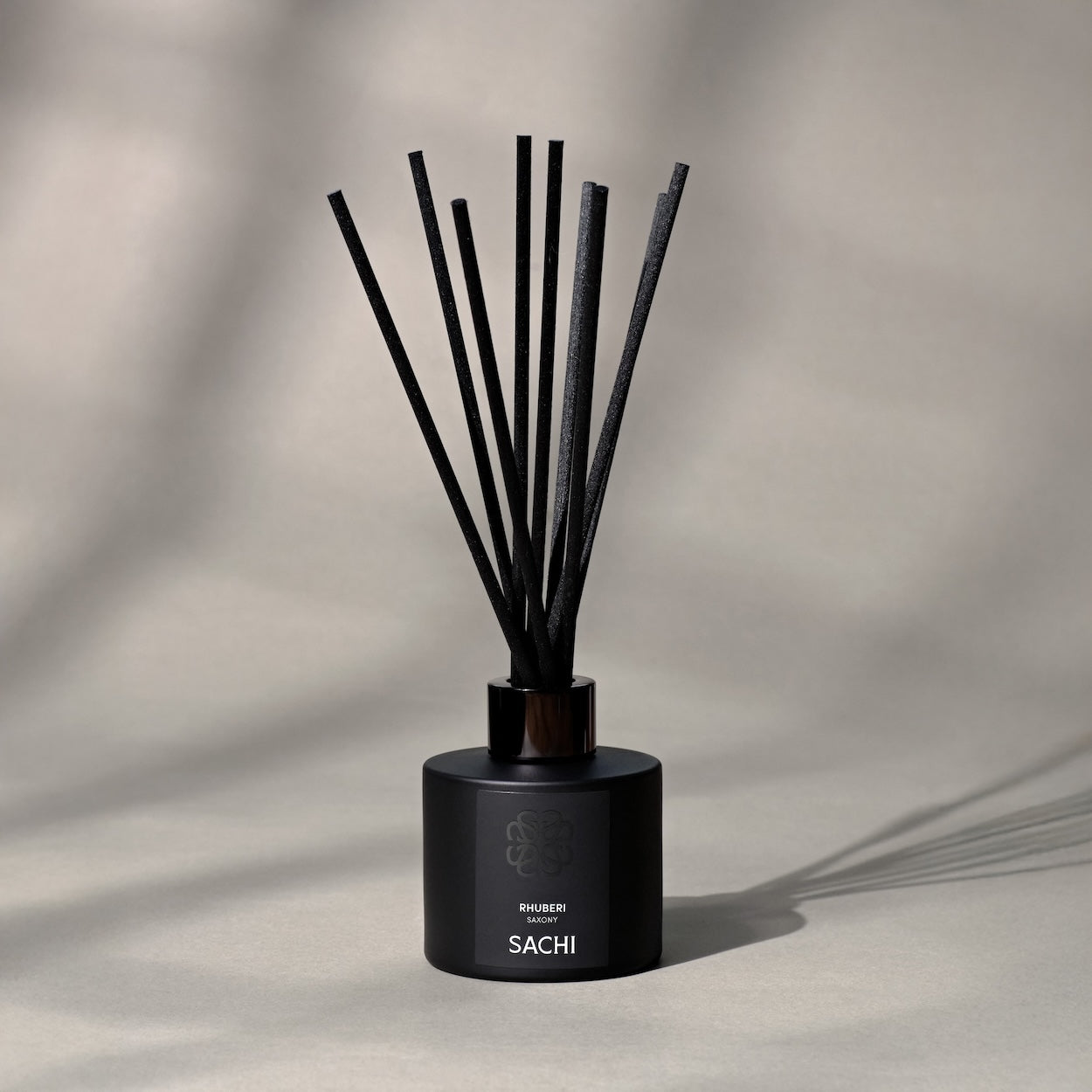 Black glass jar diffuser with reeds branded by Sachi on a grey background