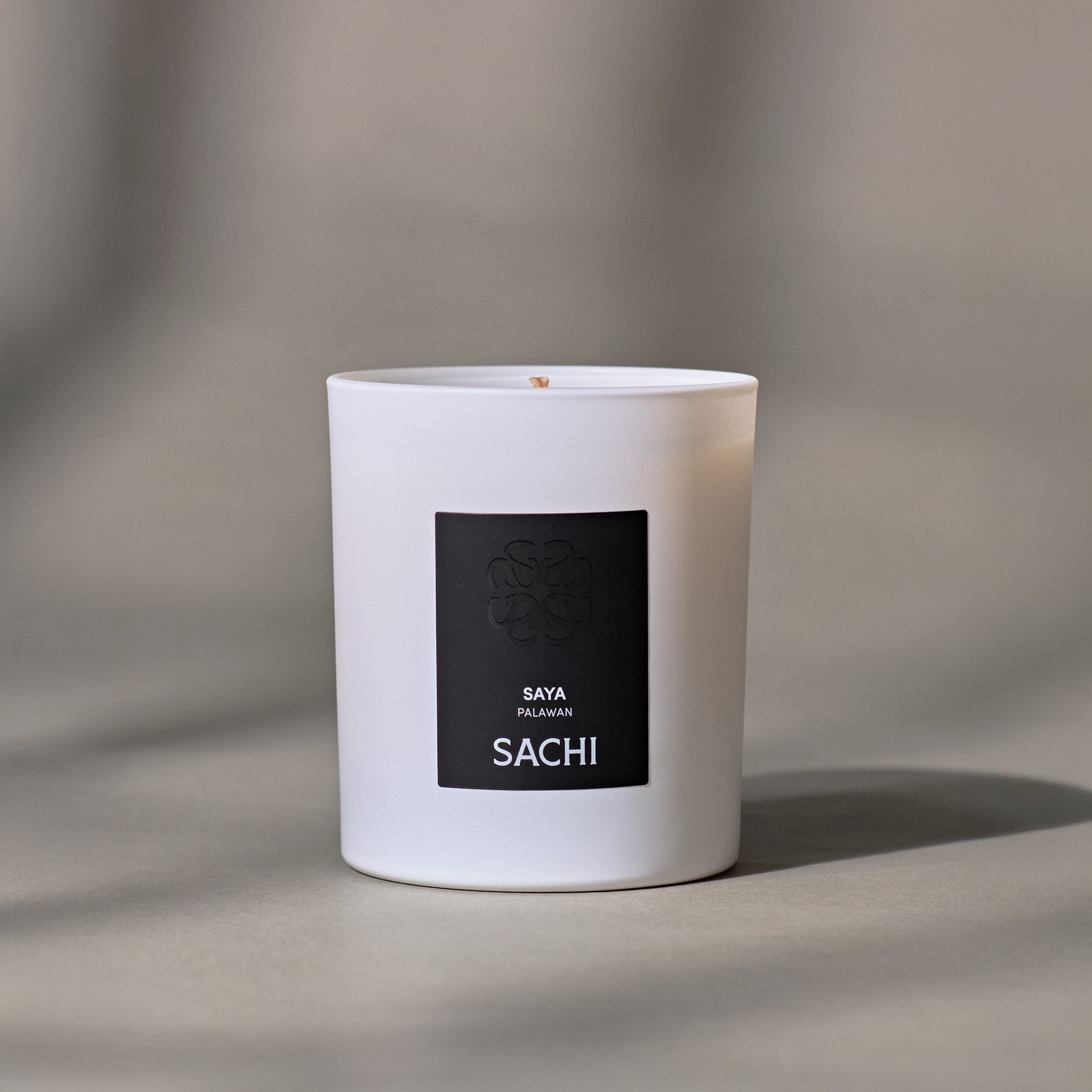 A white candle with a black label featuring the name SAYA in white text.