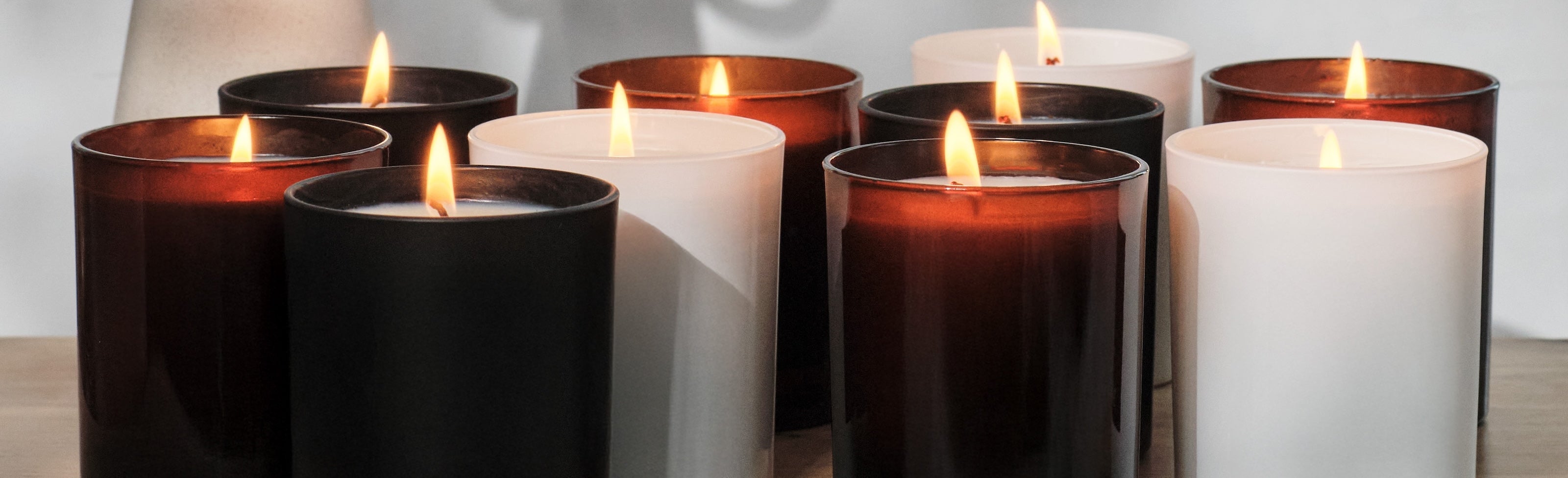 Row of lit black, white, and amber glass candles on a wooden surface.