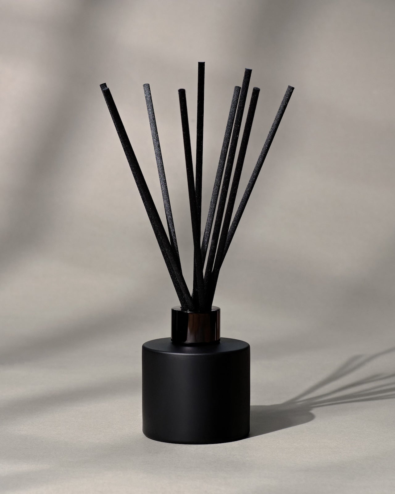 Black diffuser reeds in a black container on a neutral background