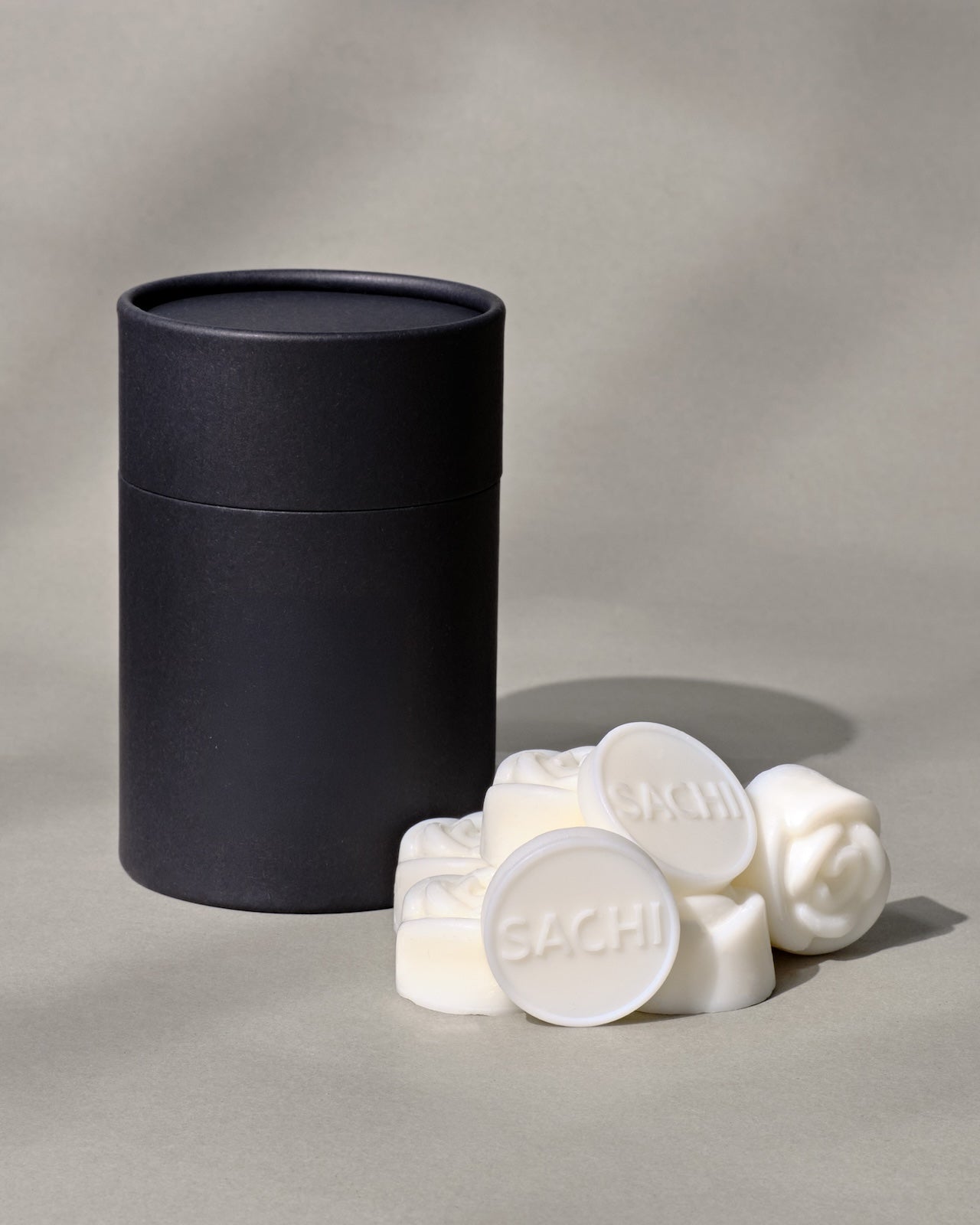 Black cylindrical container with ivory wax melts labeled 'SACHI' on a neutral background.