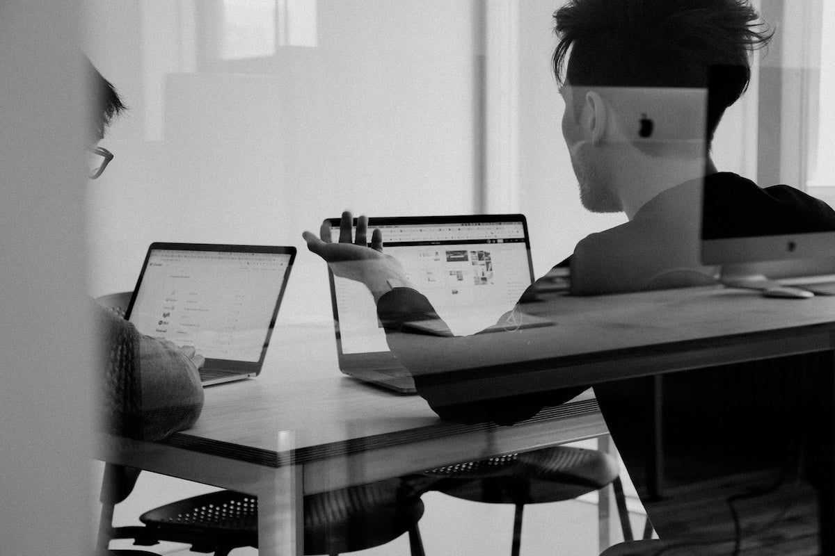 Two people working on laptops at a table in a black and white photo.