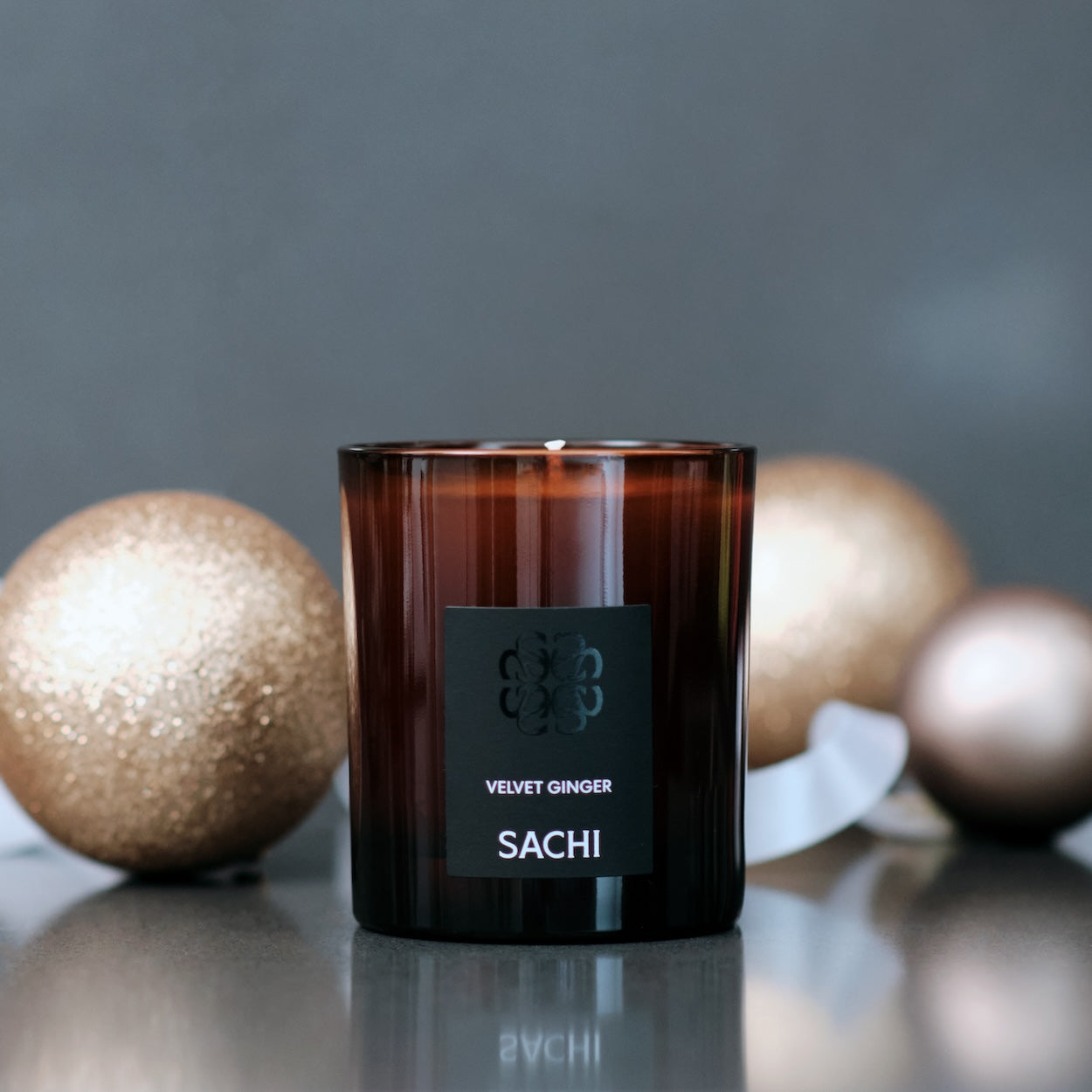 SACHI Christmas candle with decorative gold baubles on a reflective surface