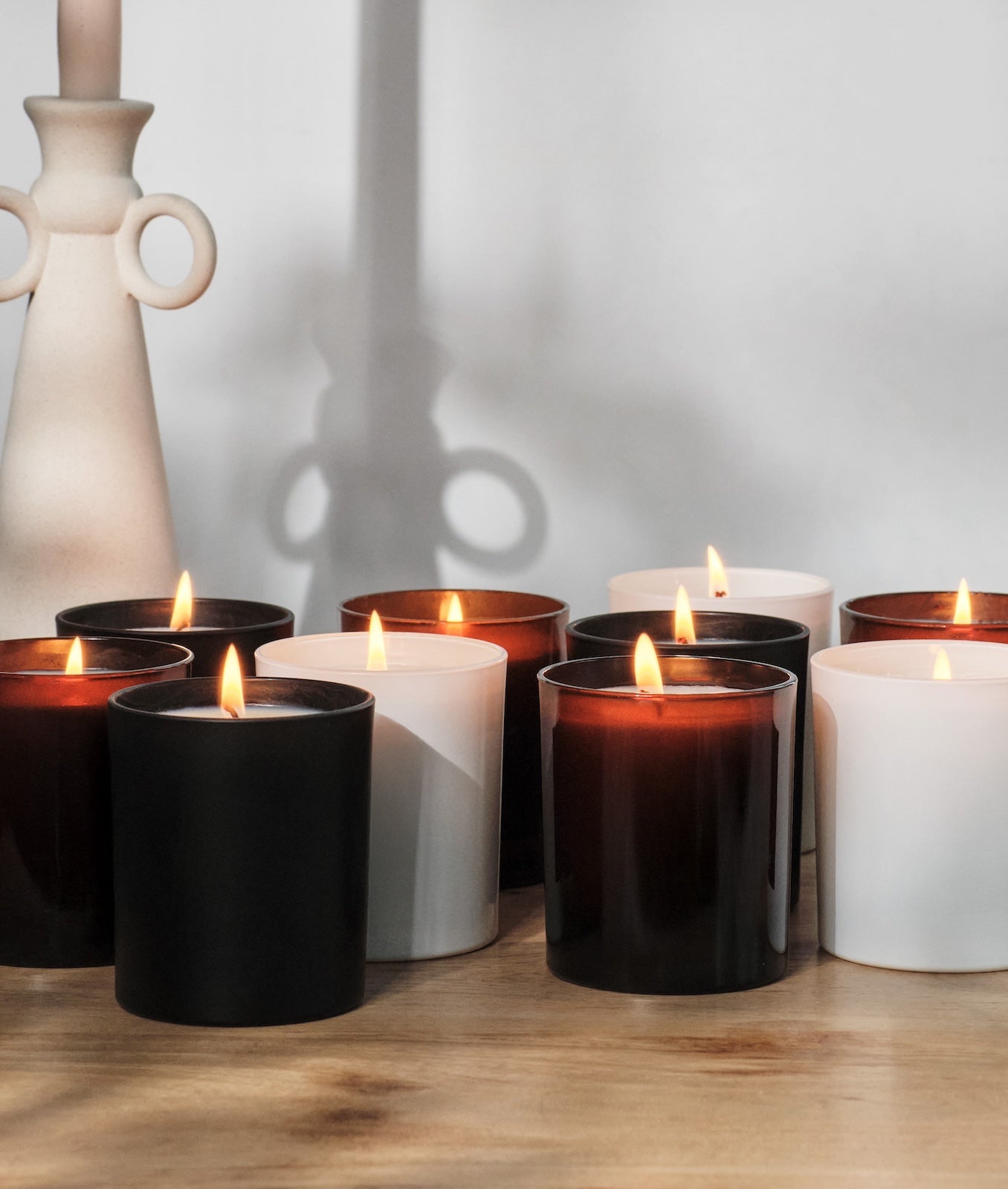 Row of lit candles in black and white containers on a wooden surface for private labels